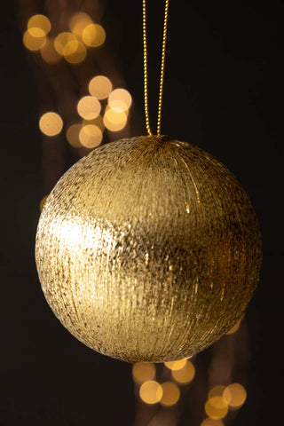 The Gold Metallic Spun Thread Christmas Bauble Decoration hanging in front of a dark background with fairy lights.