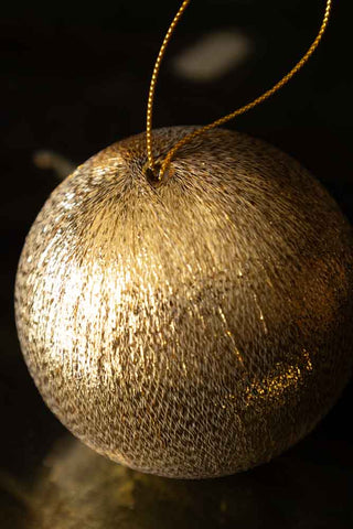 Close-up of the Gold Metallic Spun Thread Christmas Bauble Decoration on a dark surface.