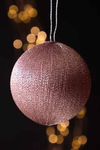 The Pink Metallic Spun Thread Christmas Bauble Decoration hanging in front of a dark background with fairy lights.