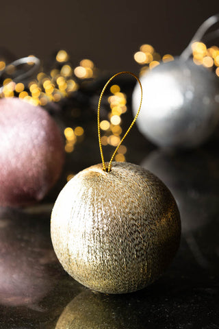 The Set Of 3 Metallic Spun Thread Christmas Bauble Decorations displayed on a dark surface with fairy lights in the background.