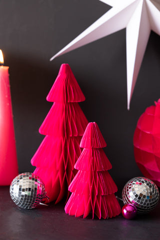 The Set Of 3 Neon Pink Paper Trees styled on a dark surface with a lit candle and some Christmas decorations.