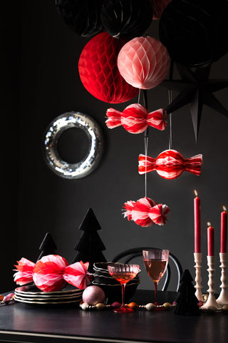 The Set Of 3 Pink & Red Honeycomb Sweets hanging as part of a decorated Christmas table, styled with lit candles, tableware and decorations.