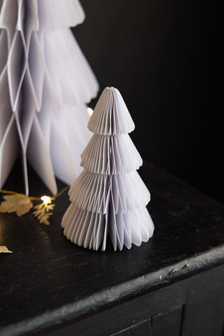 A close up image of the small tree in the Set Of 3 White Paper Trees, displayed on a black surface with some fairy lights in the background.