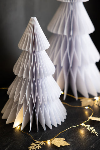 A close up image of the medium tree in the Set Of 3 White Paper Trees, displayed on a black surface with some fairy lights in the background.