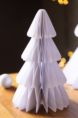 Two of the Set Of 3 White Paper Trees displayed on a wooden surface with a bauble and some fairy lights also in the shot.