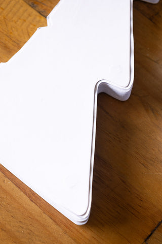 Close-up of one of the Set Of 3 White Paper Trees unassembled, displayed on a wooden surface.