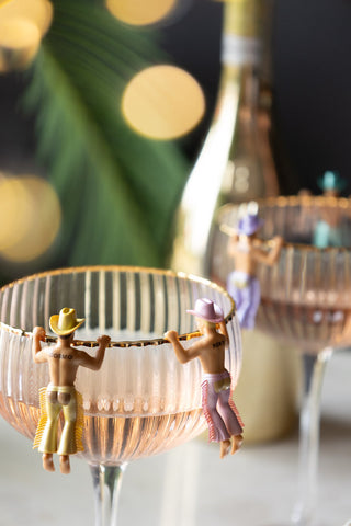 Two small plastic cowboy drink markers hanging onto the edge of a champagne coupe glass.