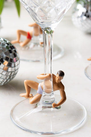 Close-up of one of the Set Of 4 Hunk Wine Glass Charms on the base of a cocktail glass, styled with other glasses and disco ball decorations.