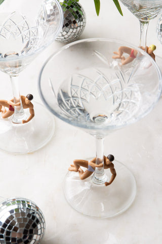 Three of the Set Of 4 Hunk Wine Glass Charms displayed on glasses, on a table with some disco ball decorations, seen from above.