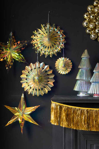 The Set Of 5 Iridescent Star Decorations displayed on a black wall next to a wreath, garland and Christmas tree decorations.