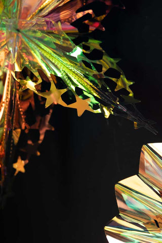 Detail shot of two of the Set Of 5 Iridescent Star Decorations in front of a dark wall.