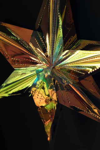 Close-up of one of the Set Of 5 Iridescent Star Decorations in front of a dark wall.