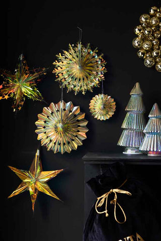 The Set Of 5 Iridescent Star Decorations styled on a dark wall next to a fireplace, with a Christmas sack, wreath and Christmas tree ornaments.