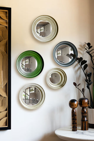 The Set Of 5 Metal Frame Mirrors in Green & Natural displayed on a neutral wall next to a framed artwork and a table with some ornaments and a potted plant on.