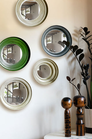 The Set Of 5 Metal Frame Mirrors in Green & Natural styled on a plain wall above some ornaments and a potted plant on the table.