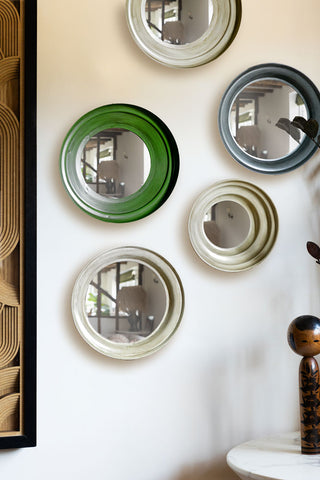 The Set Of 5 Metal Frame Mirrors in Green & Natural displayed on a white wall next to a framed artwork, ornament, plant and a table.