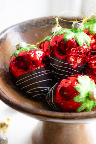 The red strawberry dipped in chocolate decorations with a green stem in a gold bowl.