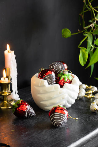 A quirky white hands bowl with a set of large strawberry decorations in the bowl.