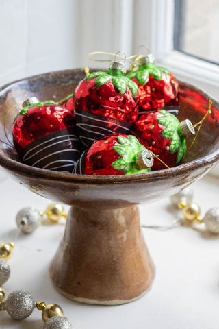 A beautiful rustic bowl filled with red strawberry decorations.