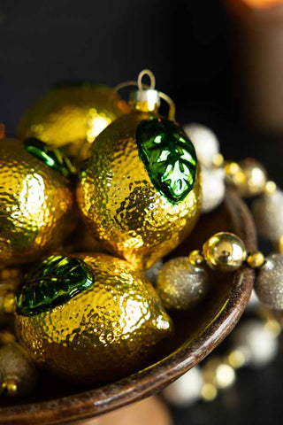 A stack of lemon shape christmas tree decorations in a rustic bowl.