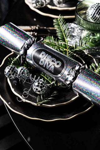 Close-up image of the Set Of 6 Silver Disco Christmas Crackers styled on a stack of black plates next to a small disco decoration.