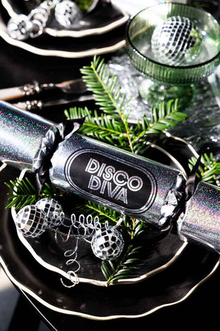 The Set Of 6 Silver Disco Christmas Crackers on a black plate on top of a small conifer branch.