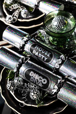 The Set Of 6 Silver Disco Christmas Crackers styled on black plates with green and disco decorations.