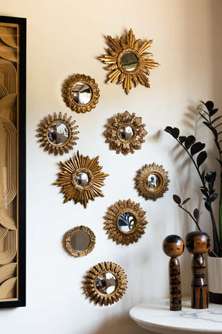 The Set Of 9 Assorted Ornate Gold Framed Mirrors arranged together on a wall, next to a framed artwork and a table with a potted plant and some wooden ornaments.