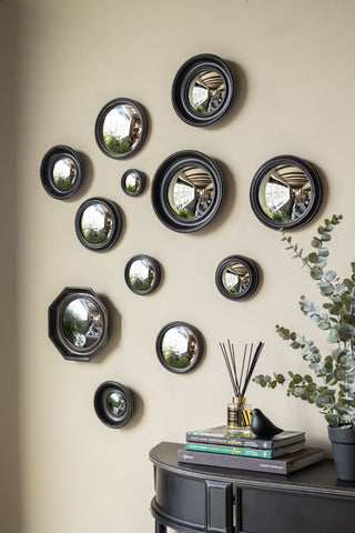 The Set of 12 Black Convex Framed Mirrors displayed on a neutrall wall above a console table styled with various home accessories.