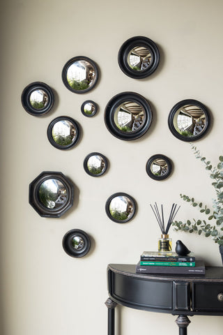 The Set of 12 Black Convex Framed Mirrors on a neutral wall, styled with a black console table with some books, a plant and some home accessories on.