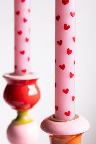 Close-up of one of the Set of 2 Red & Pink Heart Dinner Candles, displayed in a candlestick holder, with the other in the background.