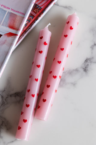 The Set of 2 Red & Pink Heart Dinner Candles on a white marble surface with some magazines.