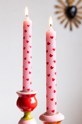 The Set of 2 Red & Pink Heart Dinner Candles lit and displayed in colourful candlestick holders.