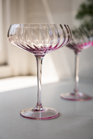 The Set of 2 Scalloped Coupe Cocktail Glasses displayed on a window ledge together.