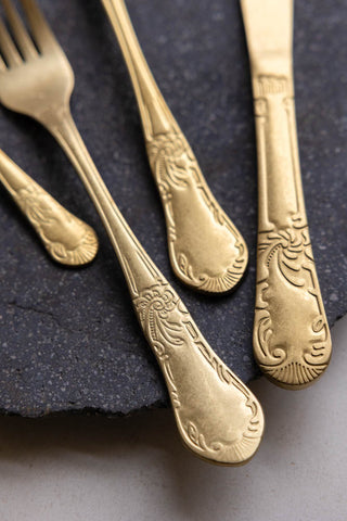 A close-up of the intricate detailing of the handles of antique-style gold forks 