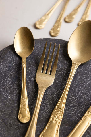 A gold teaspoon, fork and dessert spoon styled against a dark grey plate