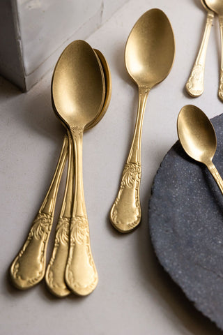 Four gold antique-style dessert spoons styled against a white tablecloth 