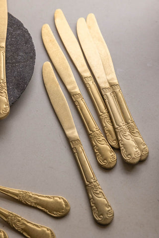 A set of five gold knives styled against a white tablecloth 