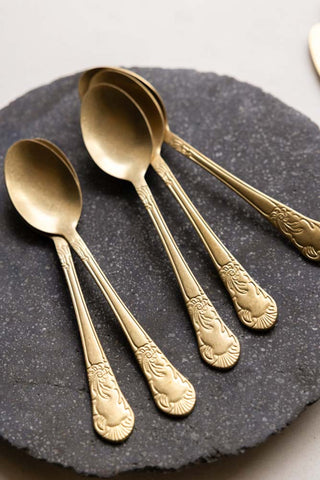 Five gold spoons set on top of a dark grey marbled plate