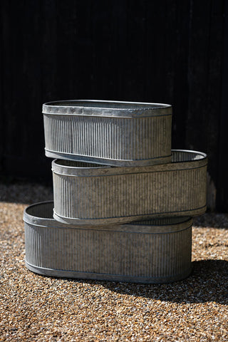 The Set of 3 Antiqued Planters displayed on stones outdoors, stacked one on top of the other.