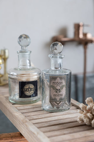 Two of the Set of 3 Apothecary-Style Poison Decanter Bottles, styled on a bath tray above a bath.