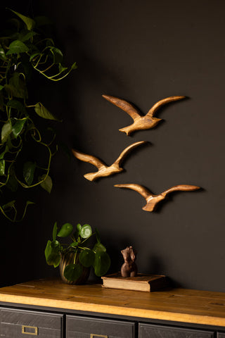 The Set of 3 Birds Wall Ornament displayed on a black wall above a sideboard, styled with plants, a book and a candle.