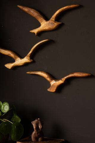 Close-up of the Set of 3 Birds Wall Ornament on a black wall, styled with a plant, book and candle.