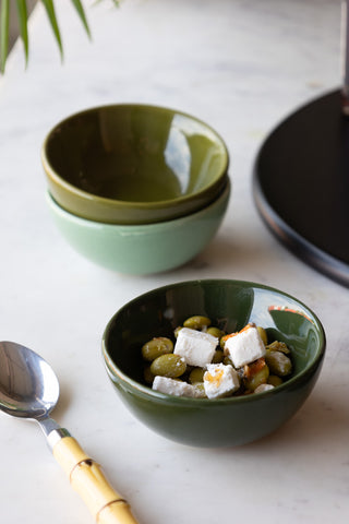 The Set of 3 Green Ceramic Dipping Bowls styled with olives and cheese inside, with a spoon and serving board.