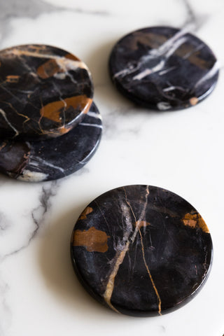 The Set of 4 Black Marble Coasters styled on a marble surface.