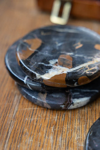 The Set of 4 Black Marble Coasters displayed on a wooden surface.