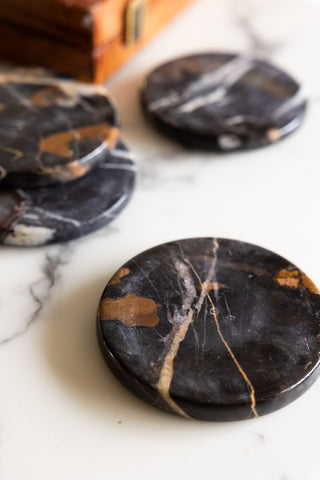 The Set of 4 Black Marble Coasters arranged on a marble surface with a wooden box in the background.