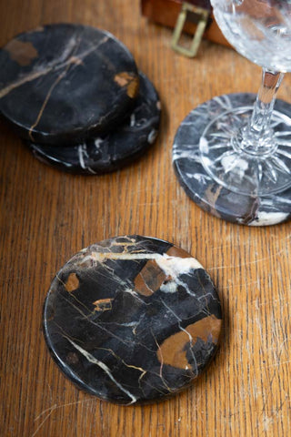 The Set of 4 Black Marble Coasters styled on a wooden surface, with a glass on one of them.