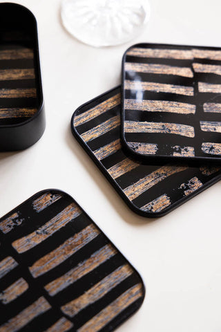 The Set of 4 Black & Gold Brushstroke Coasters With Holder displayed on a white surface.