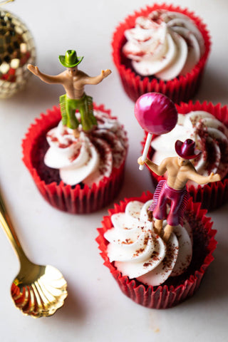 Two of the Set of 4 Cowboy Cake Toppers seen from above, styled in some cupcakes, with a spoon and gold disco ball decoration also on the table.